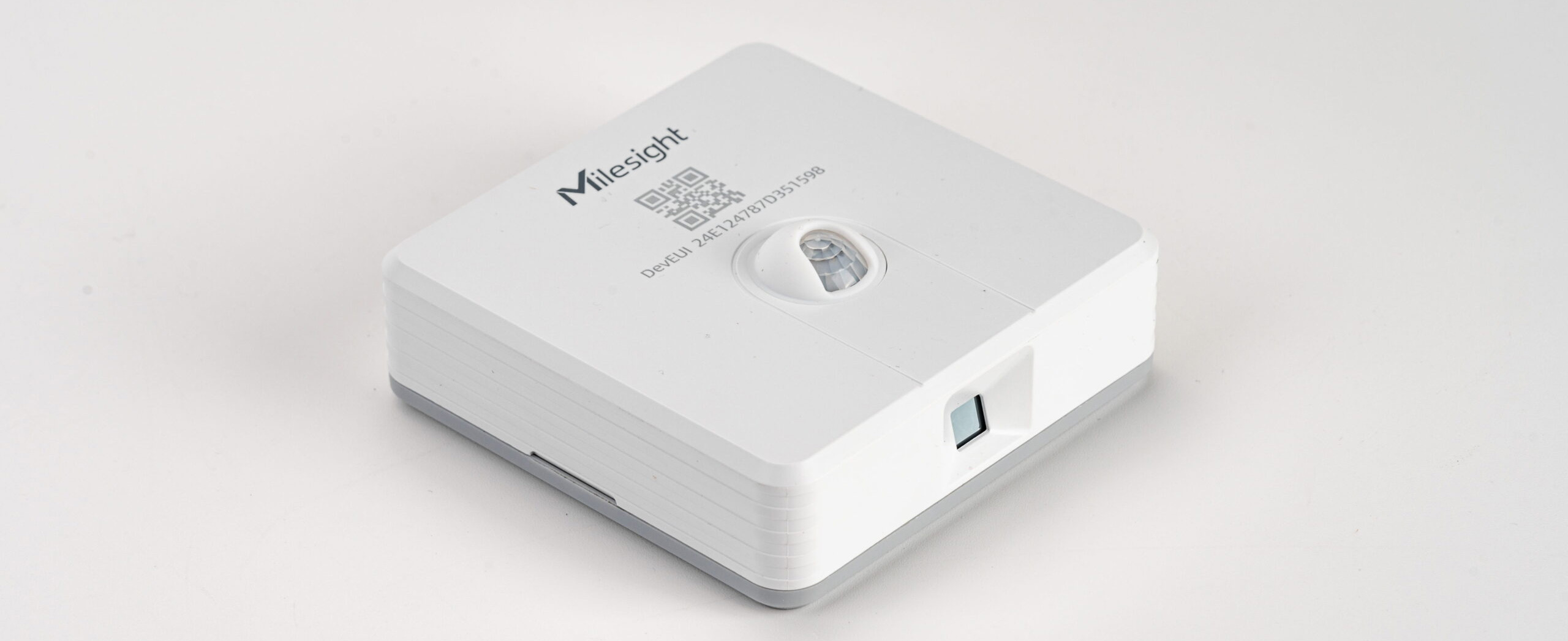 Milesight VS341 デスク占有・環境センサーの製品外観。オフィスのデスク天板裏に目立たないよう設置された超小型の白いデバイス。赤外線と温度変化を検知するデュアル技術により、正確な空席情報をリアルタイムで発信している利用イメージ。